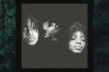 Black and White photo of three individuals - musicians. Only the faces are visible. The photo is set over a close up image of an evergreen tree. The overall colors are dark and moody.