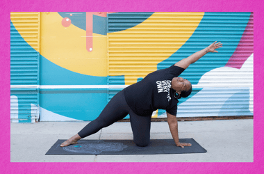 A photo of yoga instructor DuShaun in a yoga pose. DuShaun is in front of a colorful mural. Colors include fuchsia, blue, yellow and white,