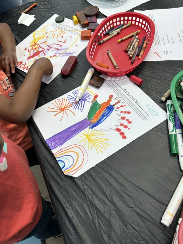 table with child hands coloring a page surrounded by crayons