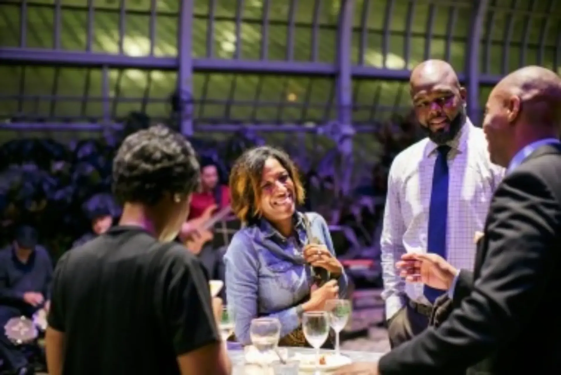 Guests socializing at cocktail reception in conservatory with purple lighting