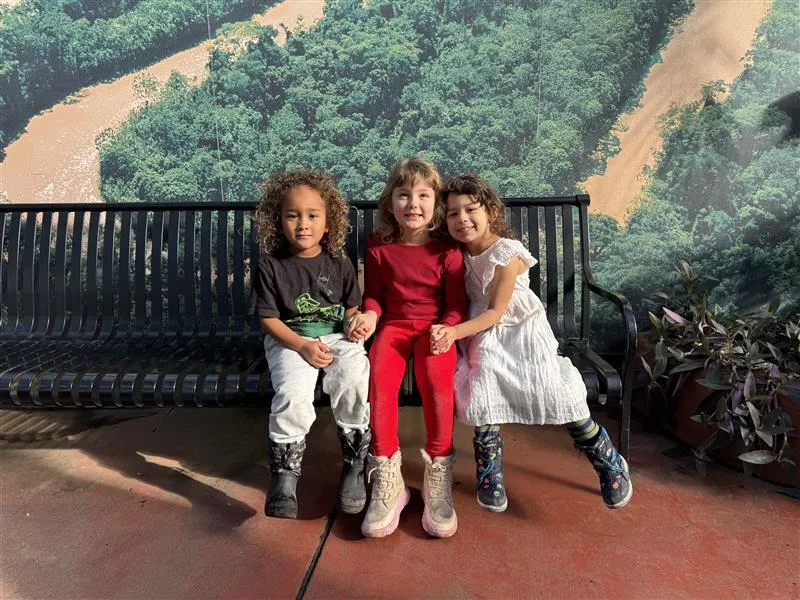 Three children sitting on a bench in the Palm Room.