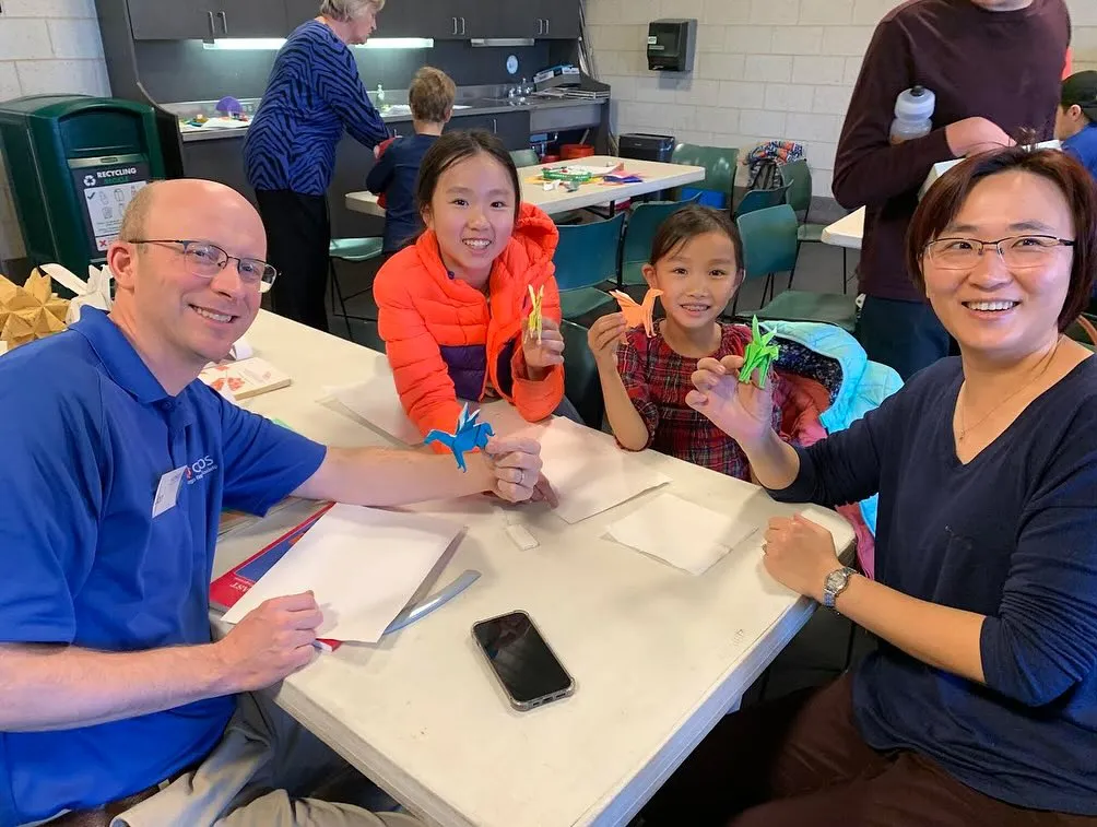 Four people, two adults, and two kids, holding up origami winged horses while sitting at a table