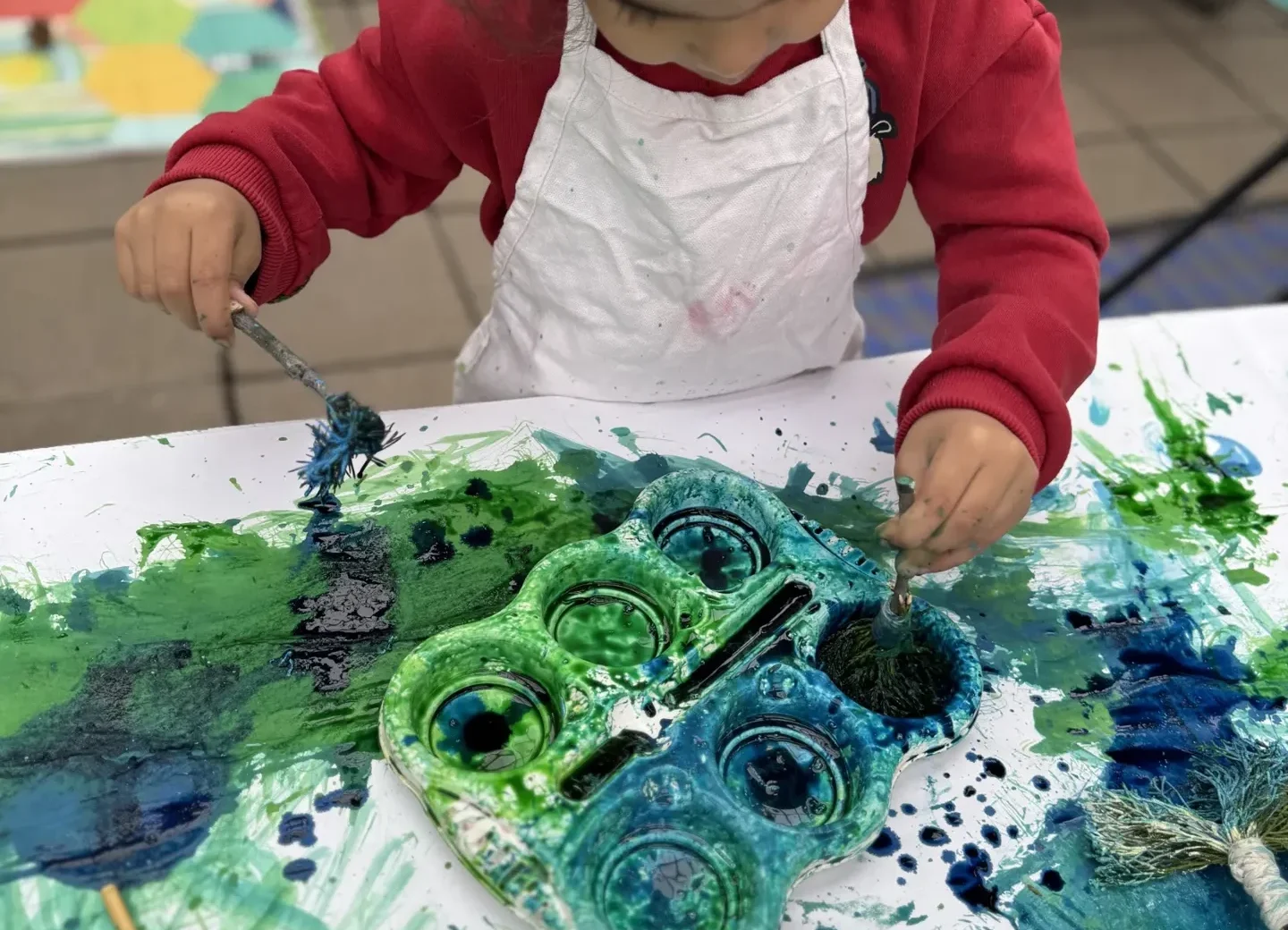 Child painting at a table covered in green and blue paint.
