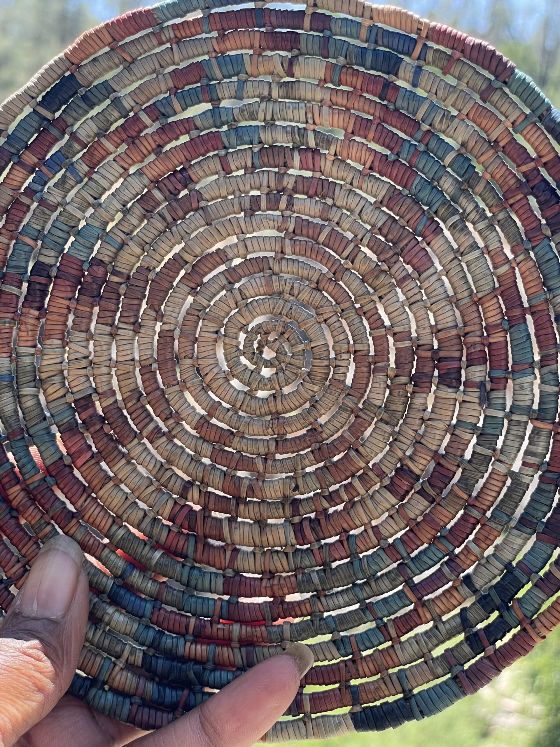 a woven pine needle basket help by a hand up to the sunlight