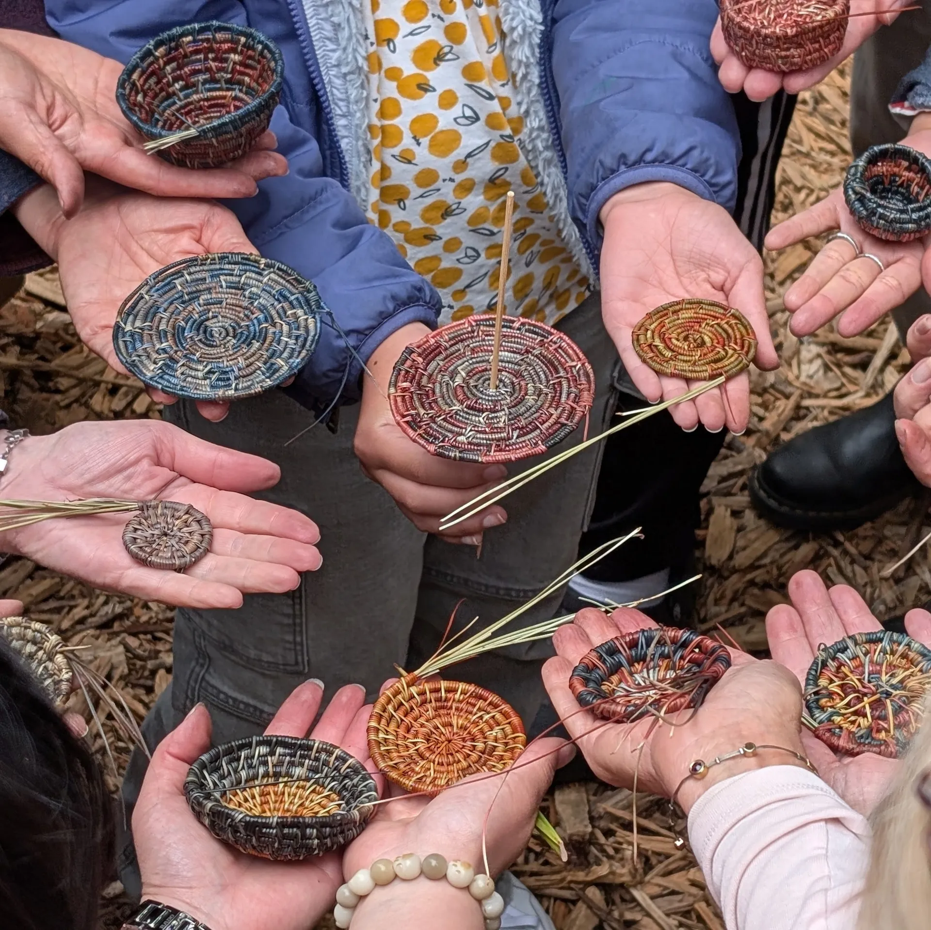 ten hands holding in-progress pine needle baskets