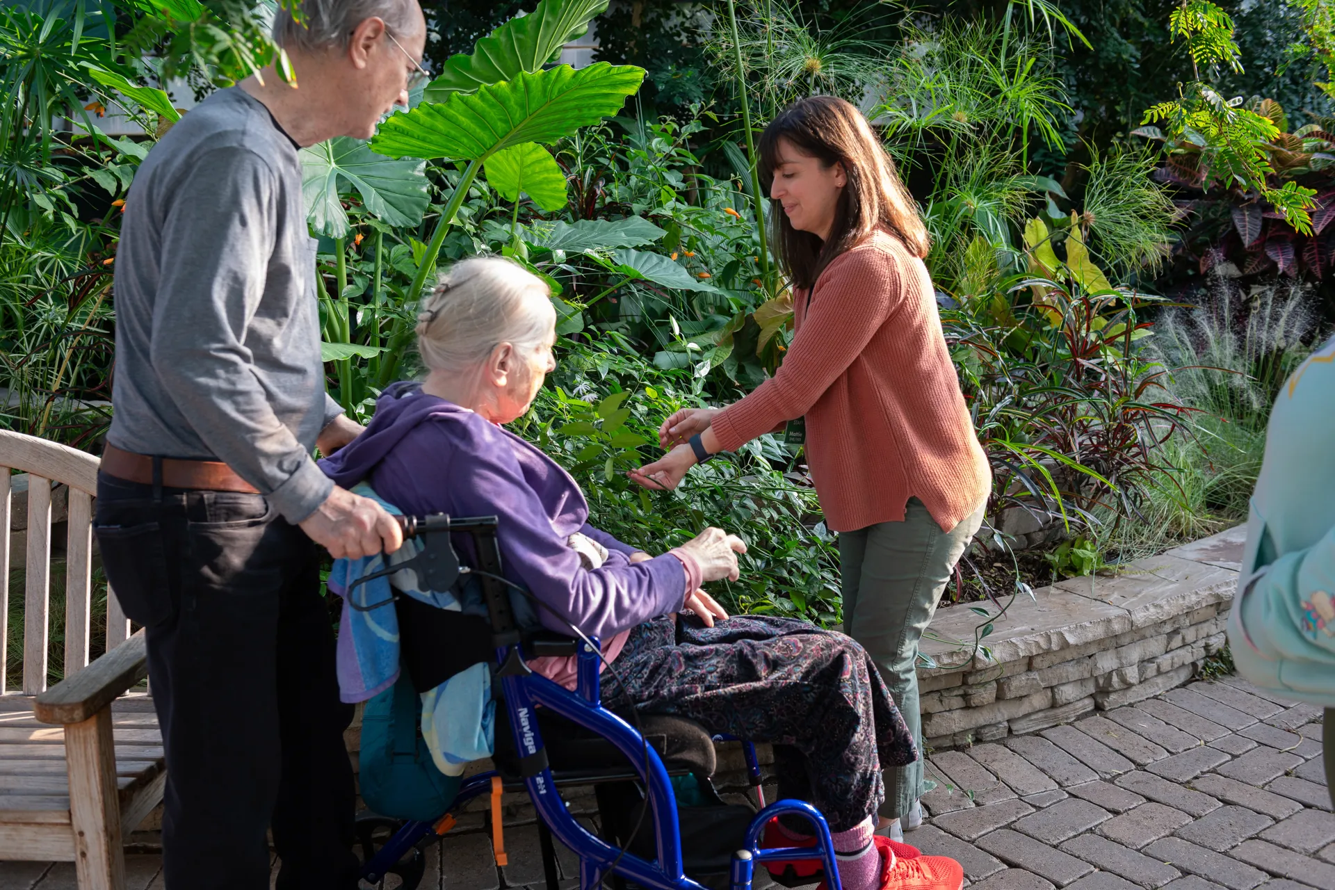 A woman in a red sweater give a tour to a woman who uses a wheel chair and a man pushing the wheelchair.
