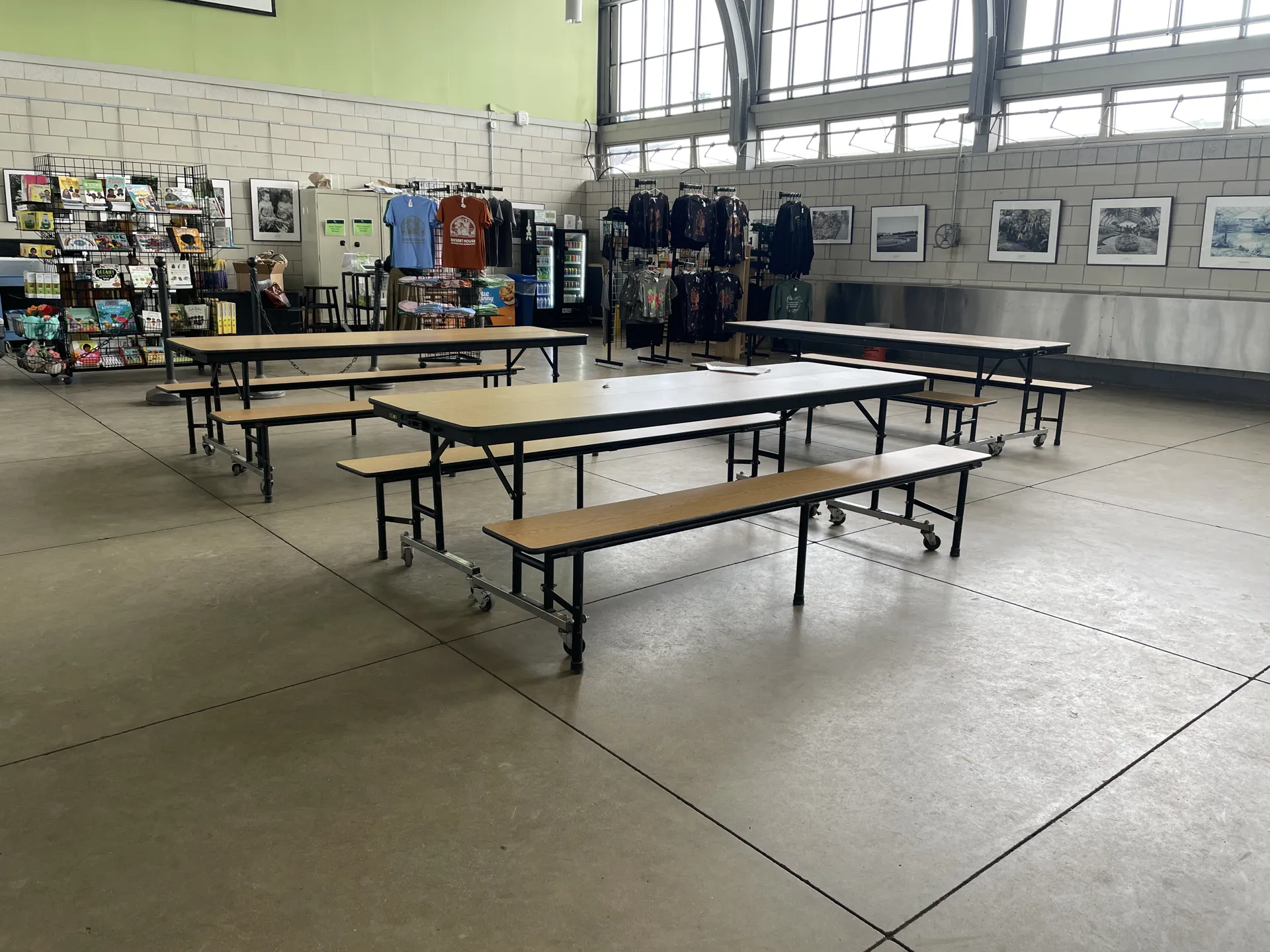 Photo of the Jensen Room with the school picnic bench lunch tables in the front, and merchandise on racks in the temporary gift shop in the back of the room.