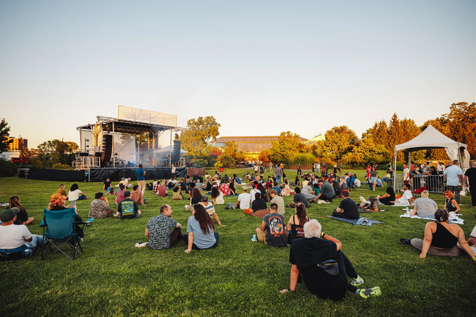 Groups of people are gathered on picnic blankets in the City Garden, listening to live music at Plantasia.