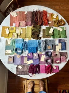 A circular marble table with examples of naturally dyed fabrics and yarn organized neatly by shades from light pink to deep purple. 