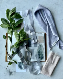 a marble table with fresh indigo leaves, a watercolor dye journal and several swaths of blue dye fabrics. 